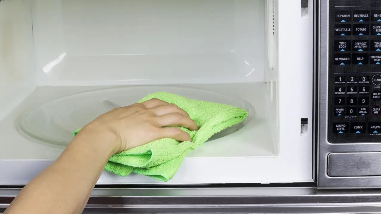 Mano con paño verde limpiando el interior de un microondas.