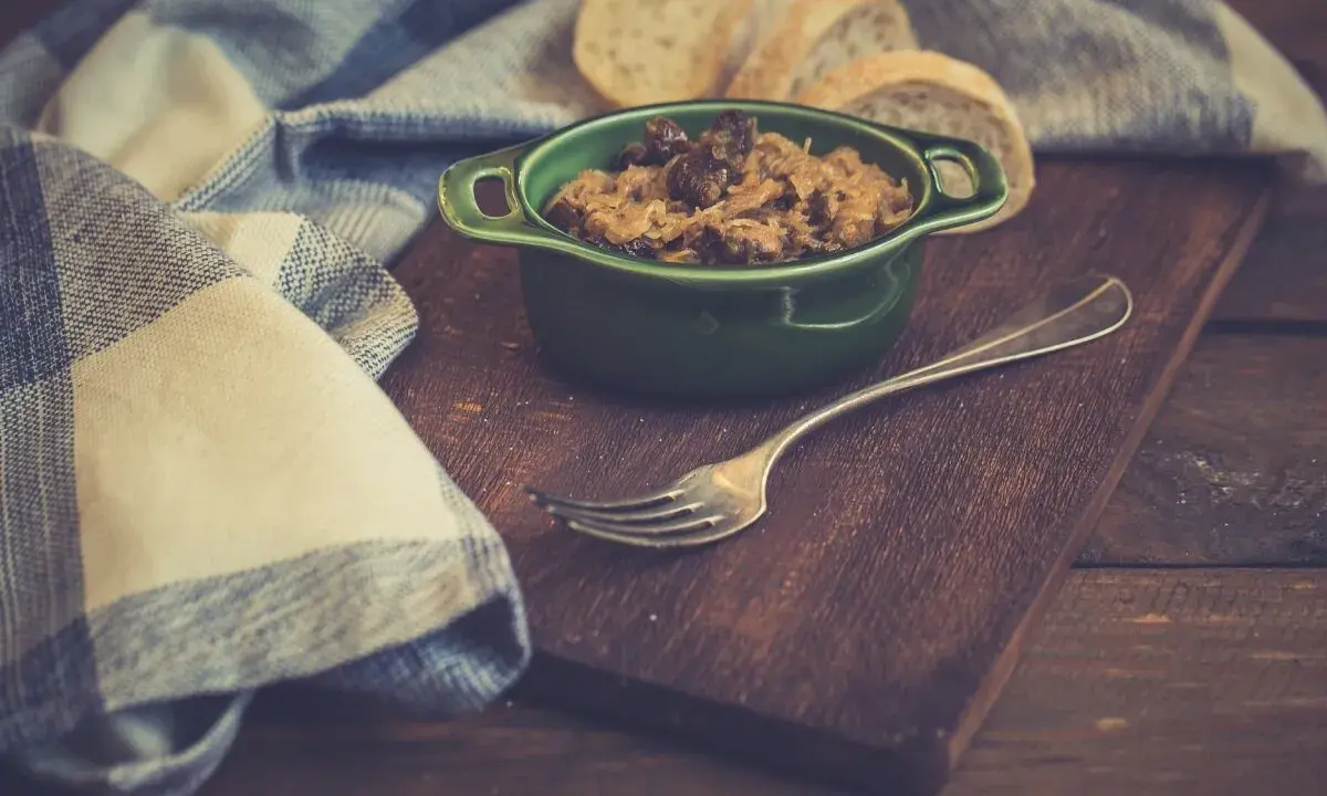 Pyszny bigos z szybkowaru w zielonej miseczce, obok kromki chleba i widelca.
