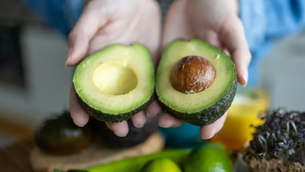 Hände halten eine aufgeschnittene Avocado. Tipps für avocado haltbar machen.