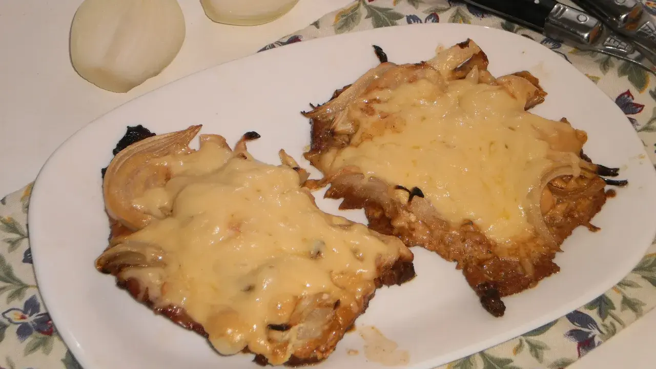 Pyszny schab w cebuli, zapieczony z serem, idealny na niedzielny obiad. Obok leżą połówki cebuli.