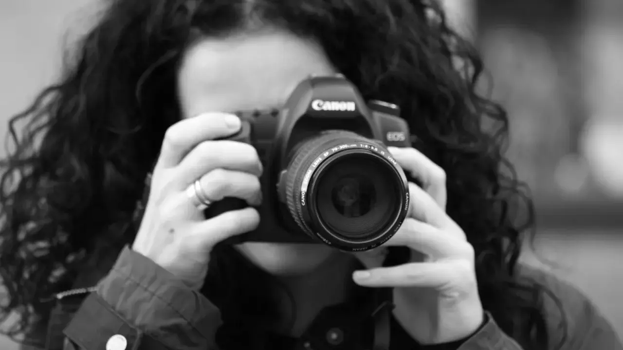Czarno-białe zdjęcie kobiety z kręconymi włosami, która trzyma aparat Canon. To jej pierwsze szkolenie z fotografii.