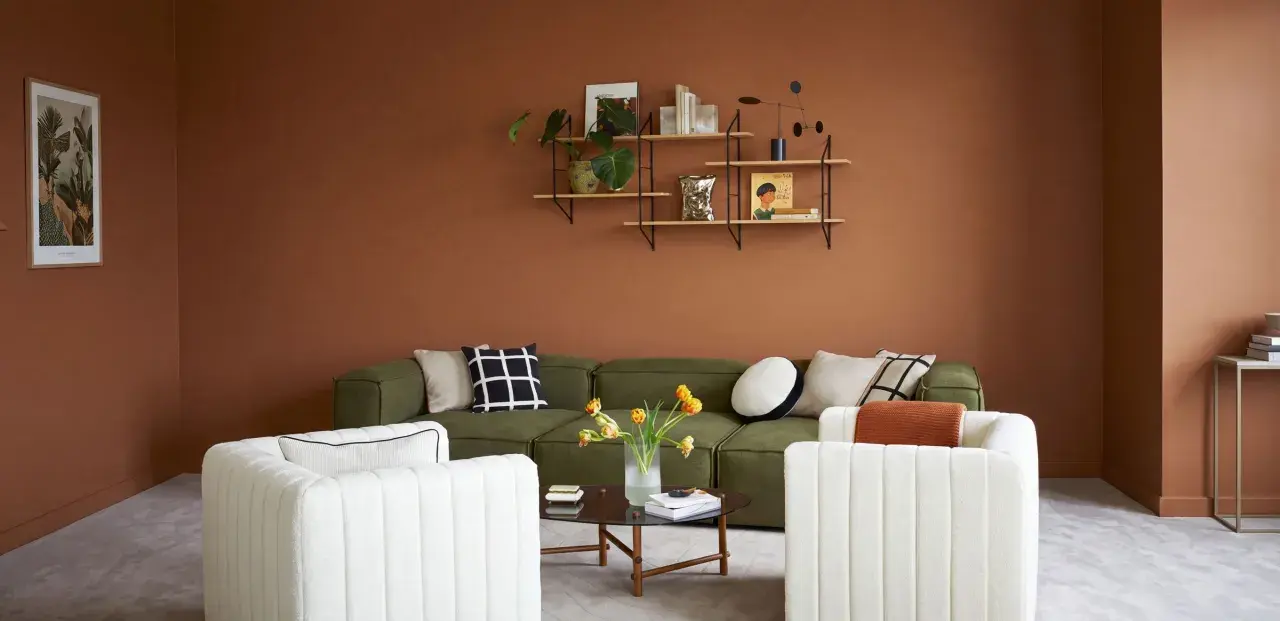 Salon cosy aux murs couleur cognac, canapé vert, fauteuils blancs et table basse.
