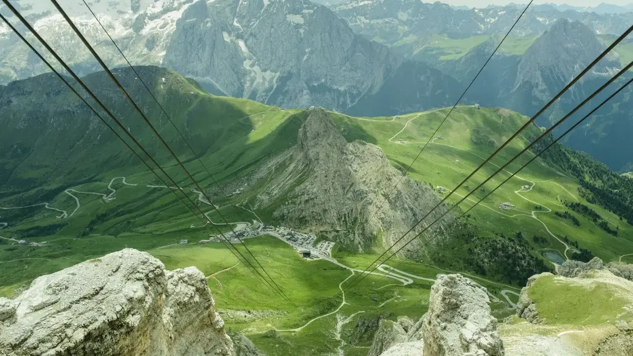 Vista mozzafiato dal passo Pordoi, con montagne innevate, verdi pendii e una strada tortuosa.