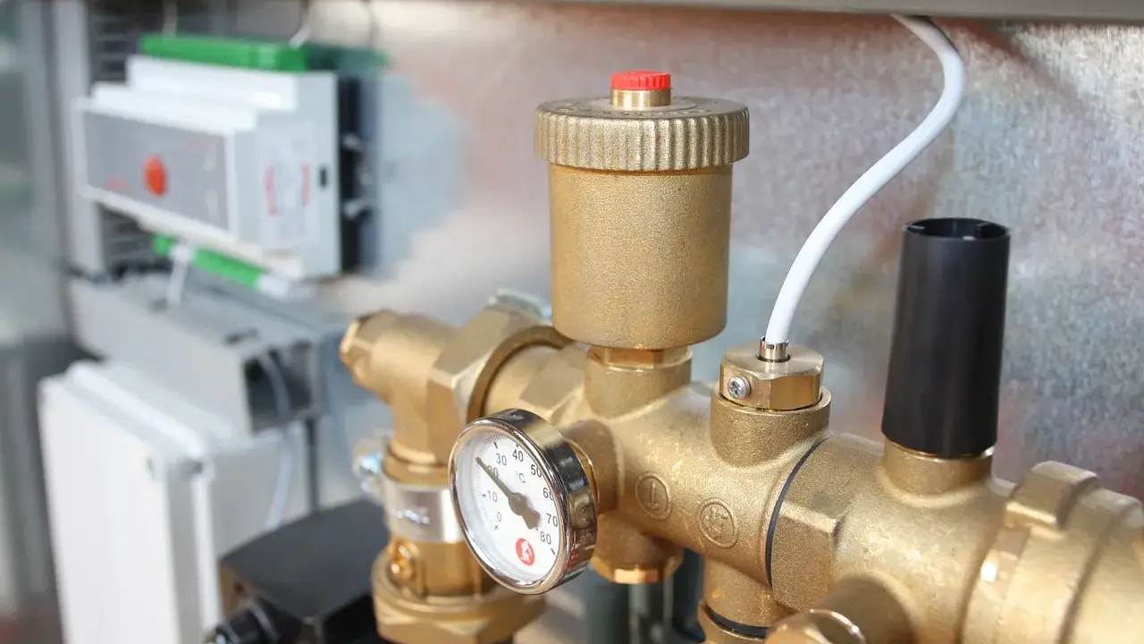 Detalle de tuberías de latón con manómetro y una válvula de seguridad. En el fondo, un panel de control.