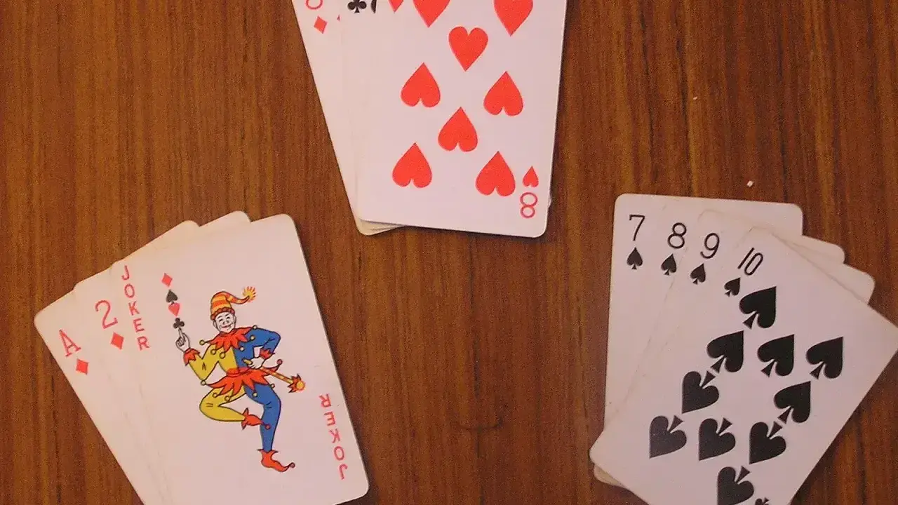 Karty na drewnianym stole: as, dwójka, joker i inne. Joker w kartach wygląda jak wesoły błazen.