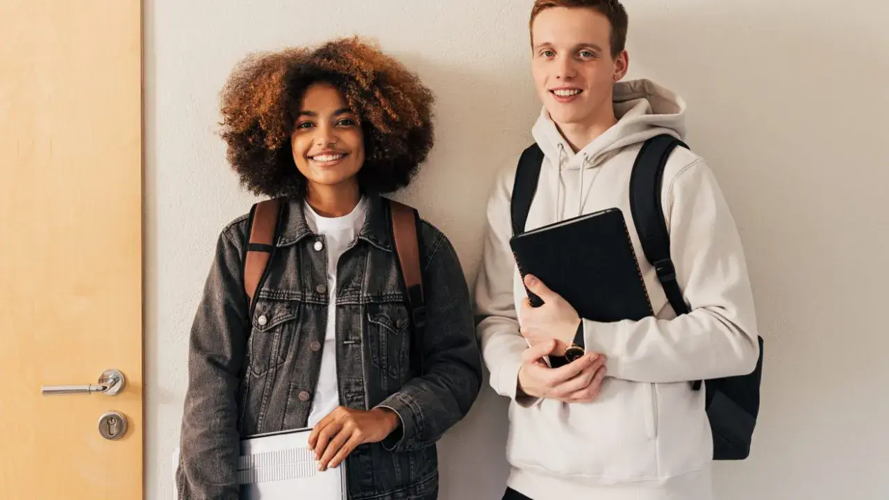 Dwóch studentów, dziewczyna z kręconymi włosami i chłopak, przygotowuje się do nauki. Może właśnie szukają informacji, jak napisać artykuł po angielsku.