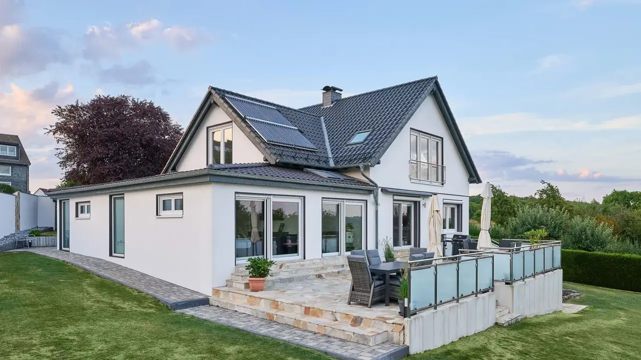 Modernes Haus mit Anbau und Terrasse. Die Solaranlage auf dem Dach deutet auf niedrige Energiekosten hin.