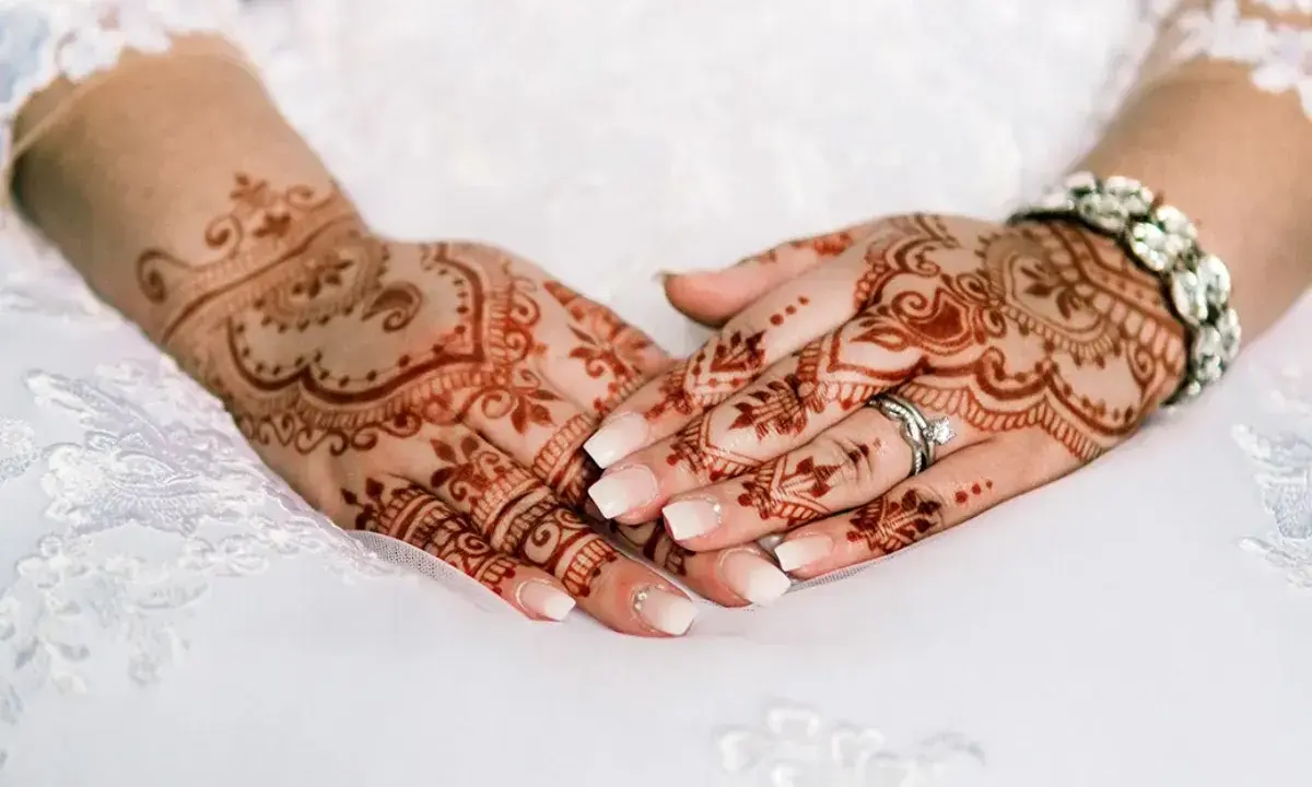 Manos de novia con intrincados diseños de henna, anillos y pulsera brillante, listas para la boda.