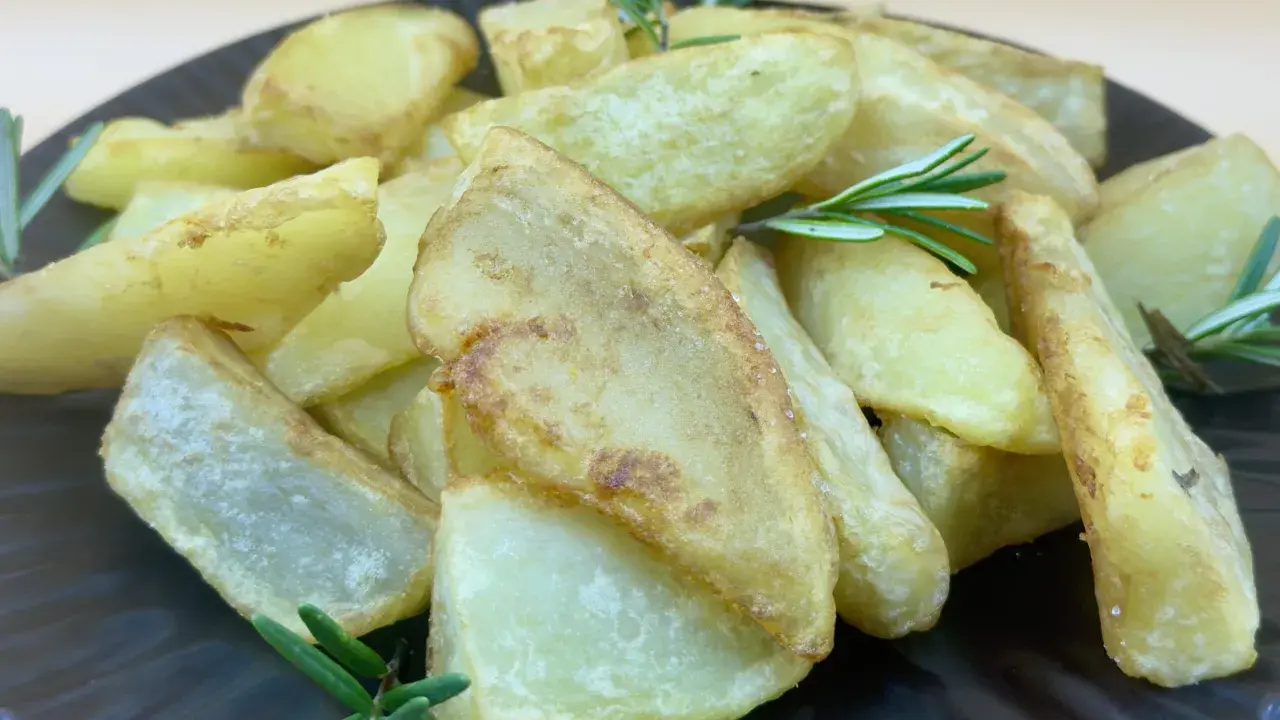Patatas gajo doradas y crujientes, adornadas con ramitas de romero fresco, servidas en un plato oscuro.