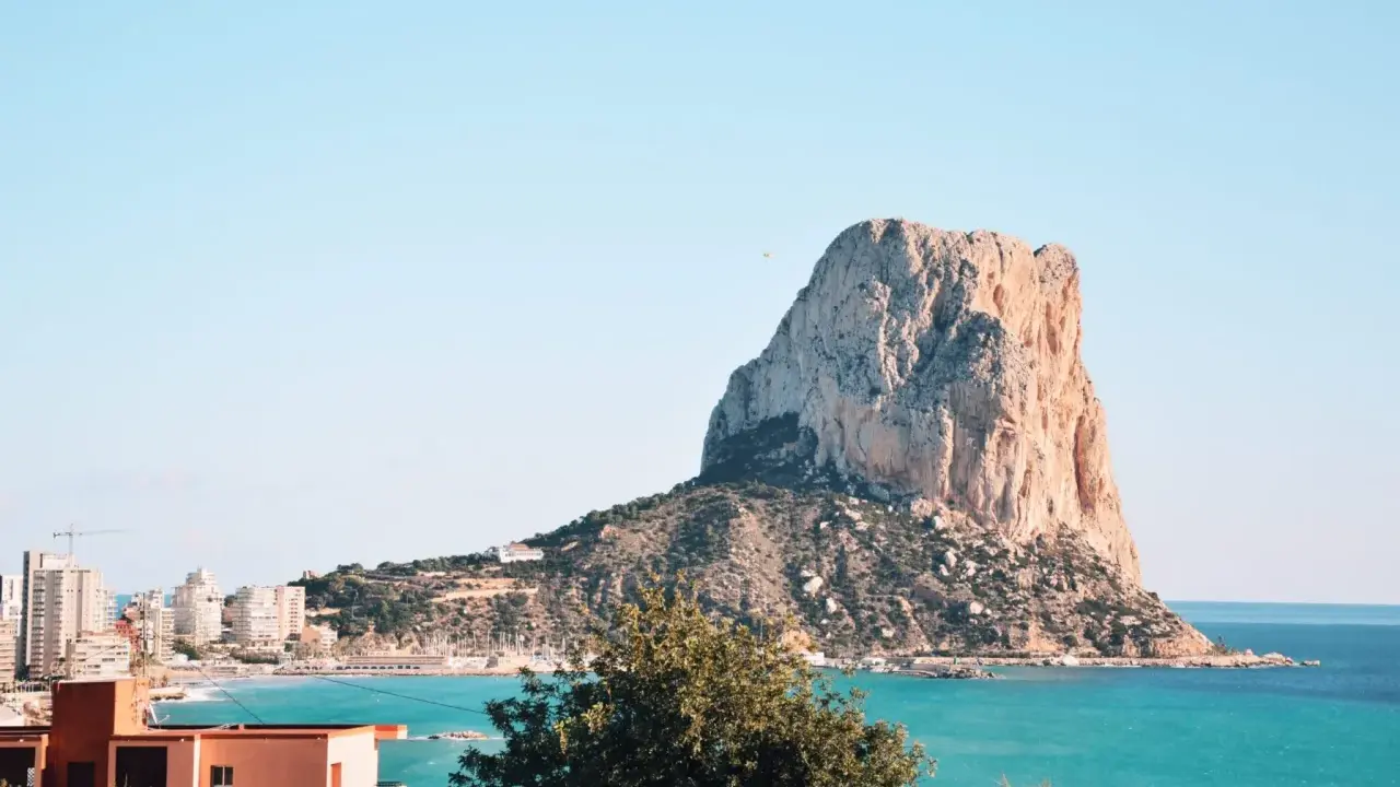 Widok na majestatyczną skałę Peñón de Ifach, symbol Costa Blanca atrakcje. Turkusowe morze i zabudowania miasta tworzą malowniczy krajobraz.