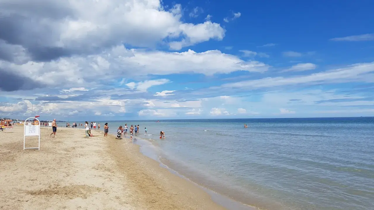 Una giornata di sole sulla spiaggia del cuore Riccione, con bambini che giocano e adulti che si godono il mare calmo sotto un cielo azzurro e nuvoloso.