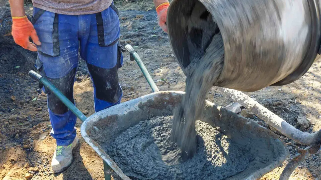 Robotnik wylewa świeży beton B25 z betoniarki do taczki. Sprawdzamy beton b25 cena za m3.