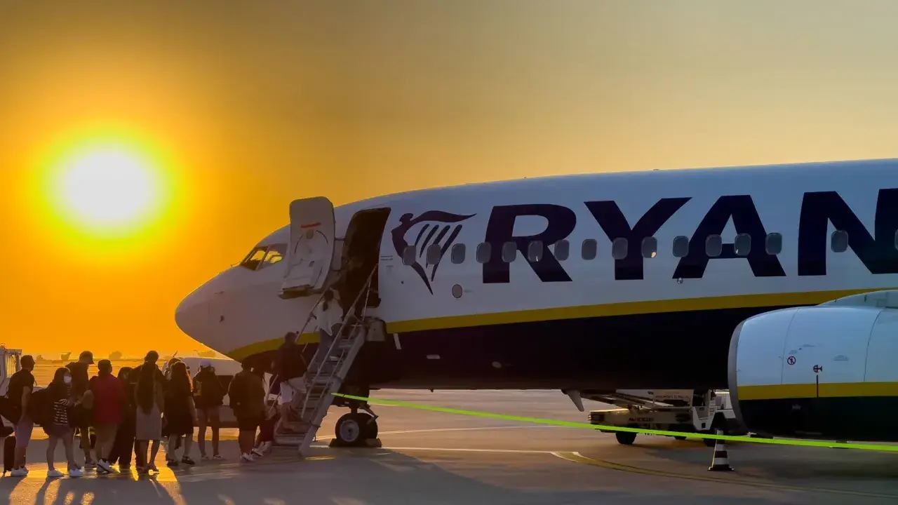 Pasażerowie wsiadają do samolotu Ryanair na tle zachodzącego słońca.