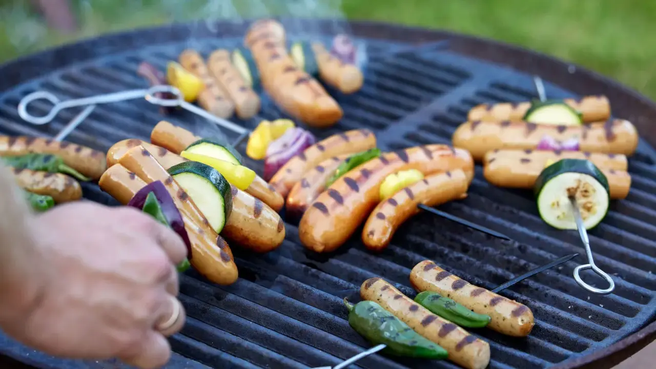 Grillad korv med grönsaker på en het grill. Röken stiger och doften sprider sig.