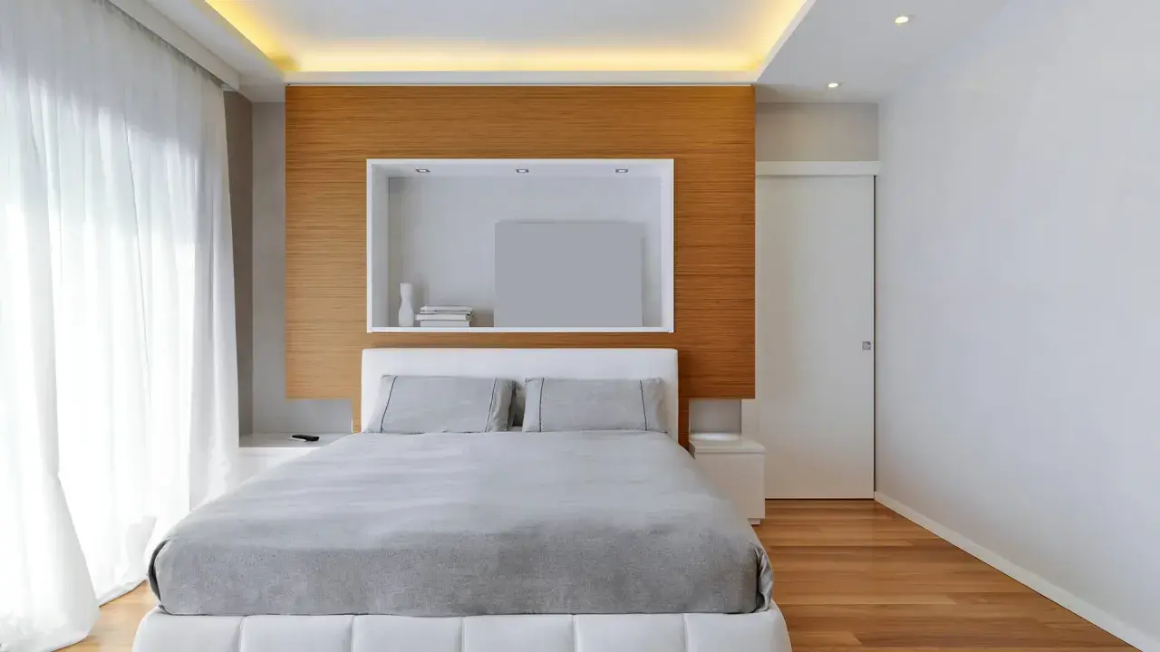 Illuminazione a scomparsa nel controsoffitto, un'idea moderna per un soffitto elegante. Camera da letto minimalista con letto bianco e testiera in legno.