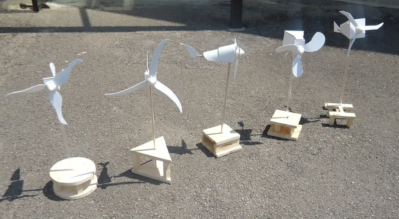 Cinq maquettes éoliennes, fabrication simple en bois, alignées sur un sol gris.