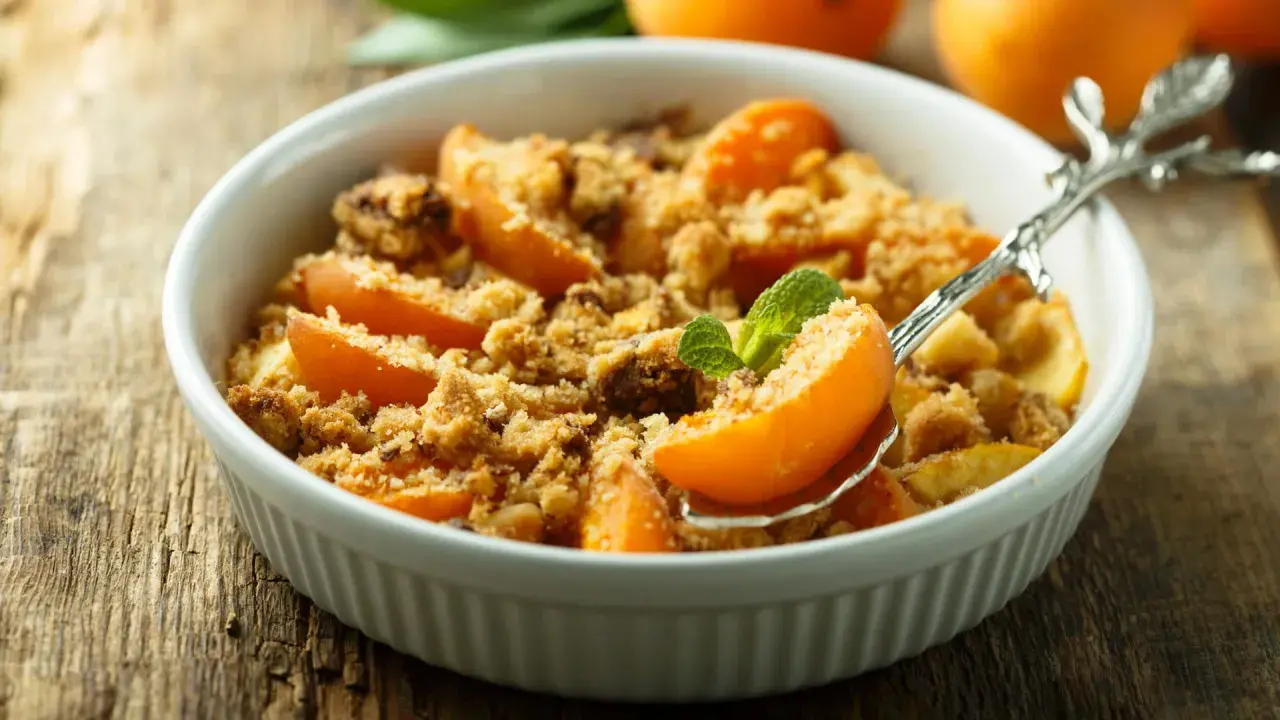 Ein köstlicher Aprikosen Crumble in einer weißen Schale, garniert mit Minze. Perfekt für einen süßen Genuss.