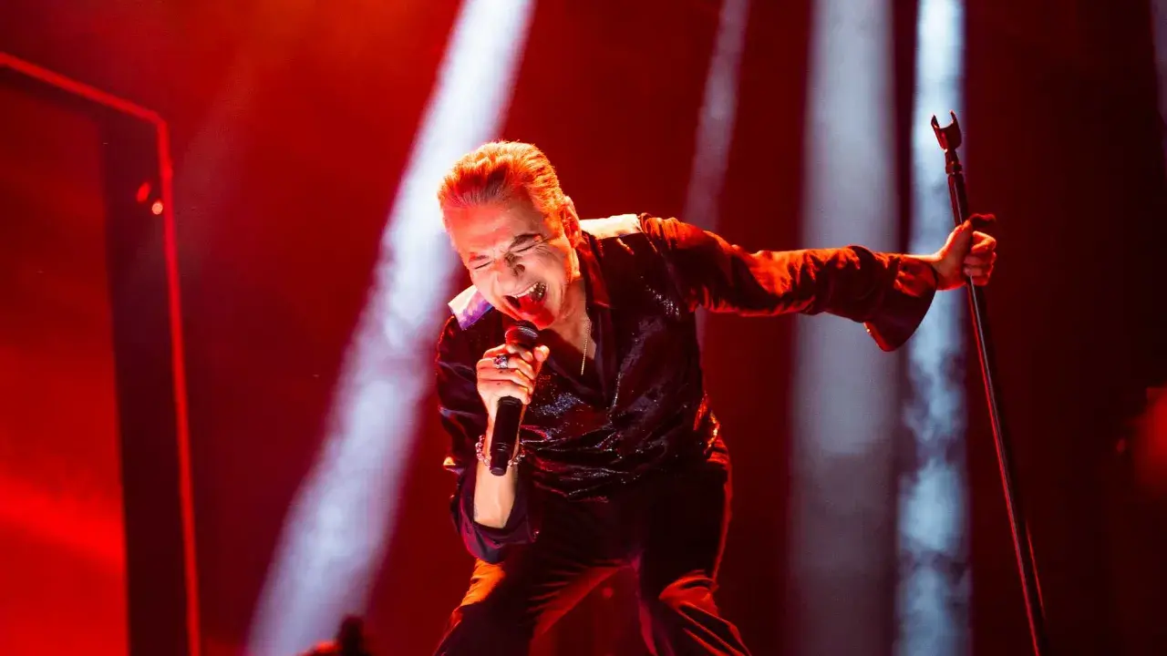 Dave Gahan sjunger passionerat under en Depeche Mode konsert, badad i rött ljus.