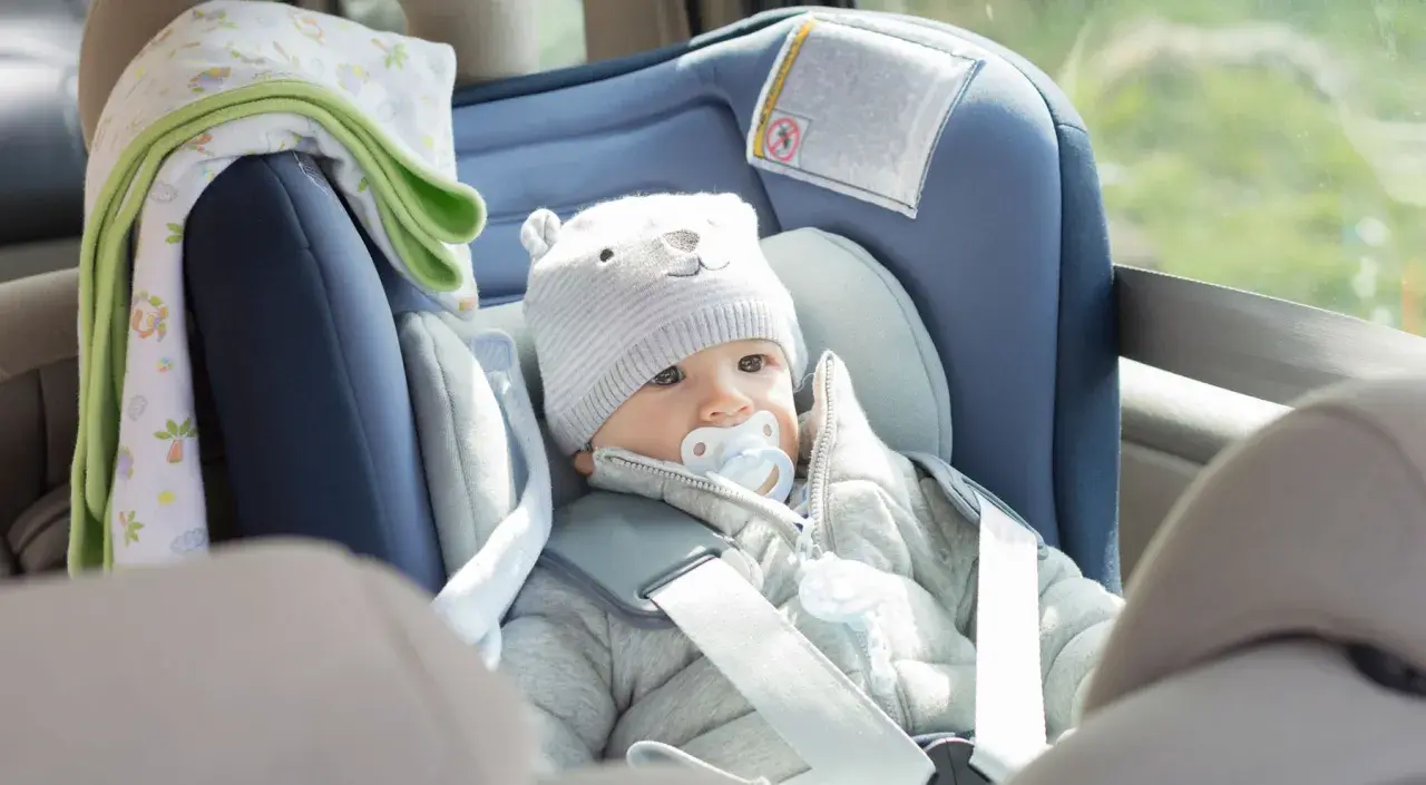Bebé con gorro de oso y chupete en un alzador o silla coche, listo para un viaje seguro.