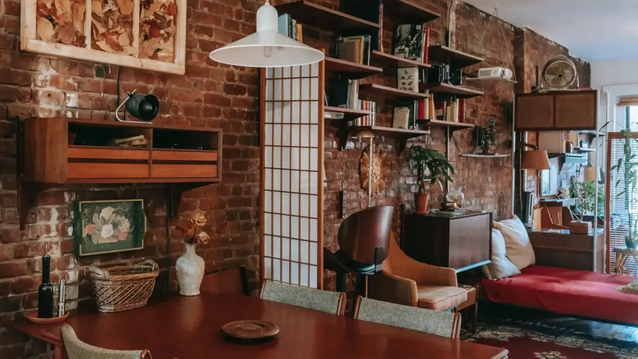 Wnętrze kawalerki z ceglaną ścianą, drewnianym stołem i meblami w stylu vintage.