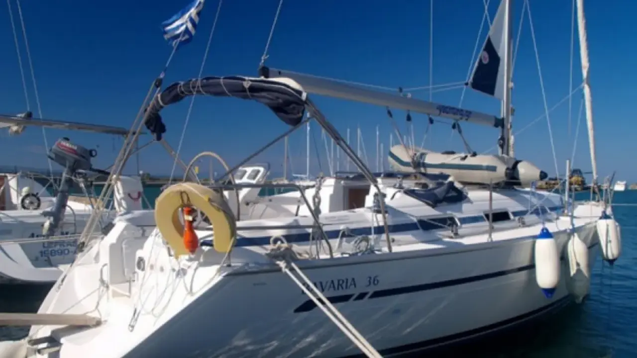 Voilier Bavaria 36 blanc amarré, pavillon grec, pare-battages bleus et blancs.