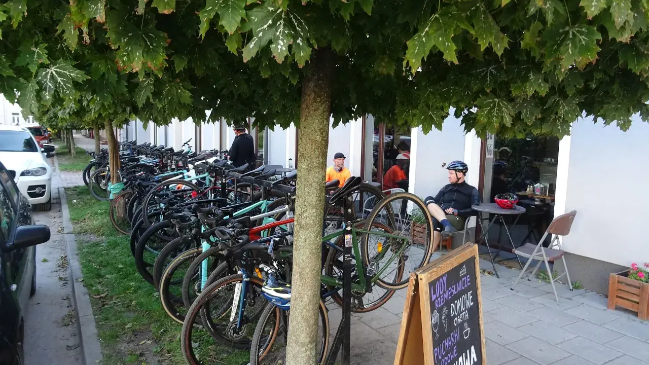 Rowerzyści odpoczywają pod drzewami w Górze Kalwarii. Rzędy rowerów czekają na dalszą trasę.