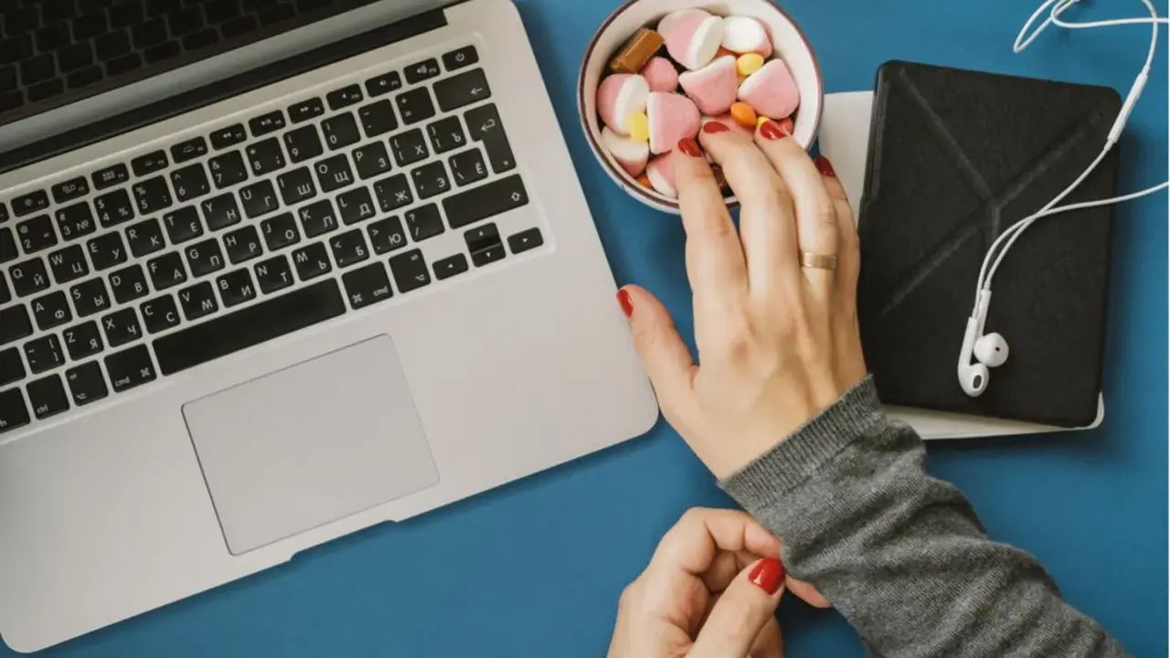 Eine Hand greift nach Süßigkeiten neben einem Laptop. Das Bild symbolisiert assoziatives Lernen: Belohnung und Fokus.