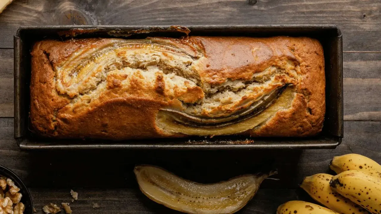 Un delizioso banana bread light appena sfornato, con banane caramellate in superficie, su un tagliere di legno.