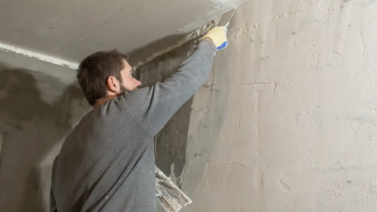 Hombre aplicando masilla en una esquina para quitar el gotele del techo.