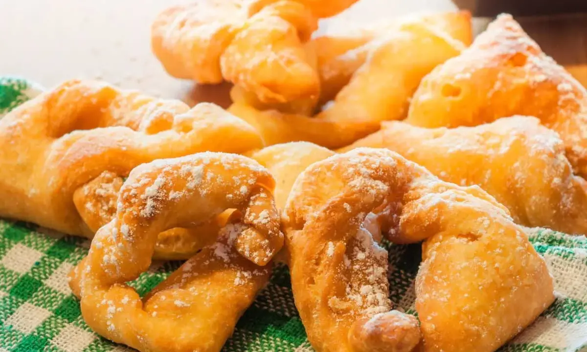 Beignets dorés saupoudrés de sucre glace sur un torchon à carreaux verts.