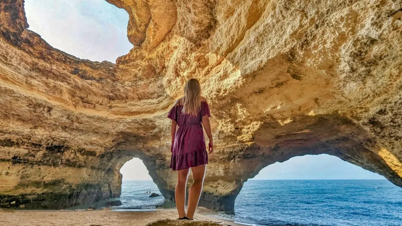 Frau steht in Höhle, blickt auf Meer. Ein Highlight der Algarve.