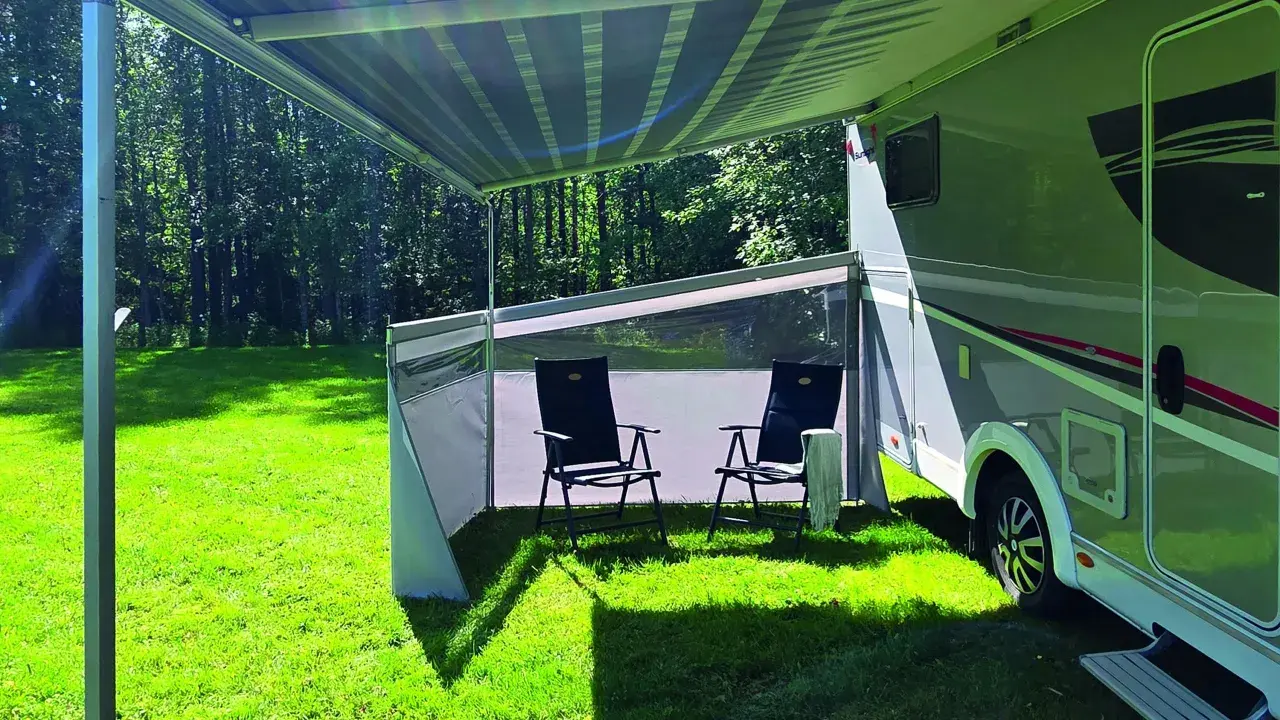 Ett vindskydd från Biltema ger skugga och skydd vid husbilen. Två stolar står redo för avkoppling i gräset.