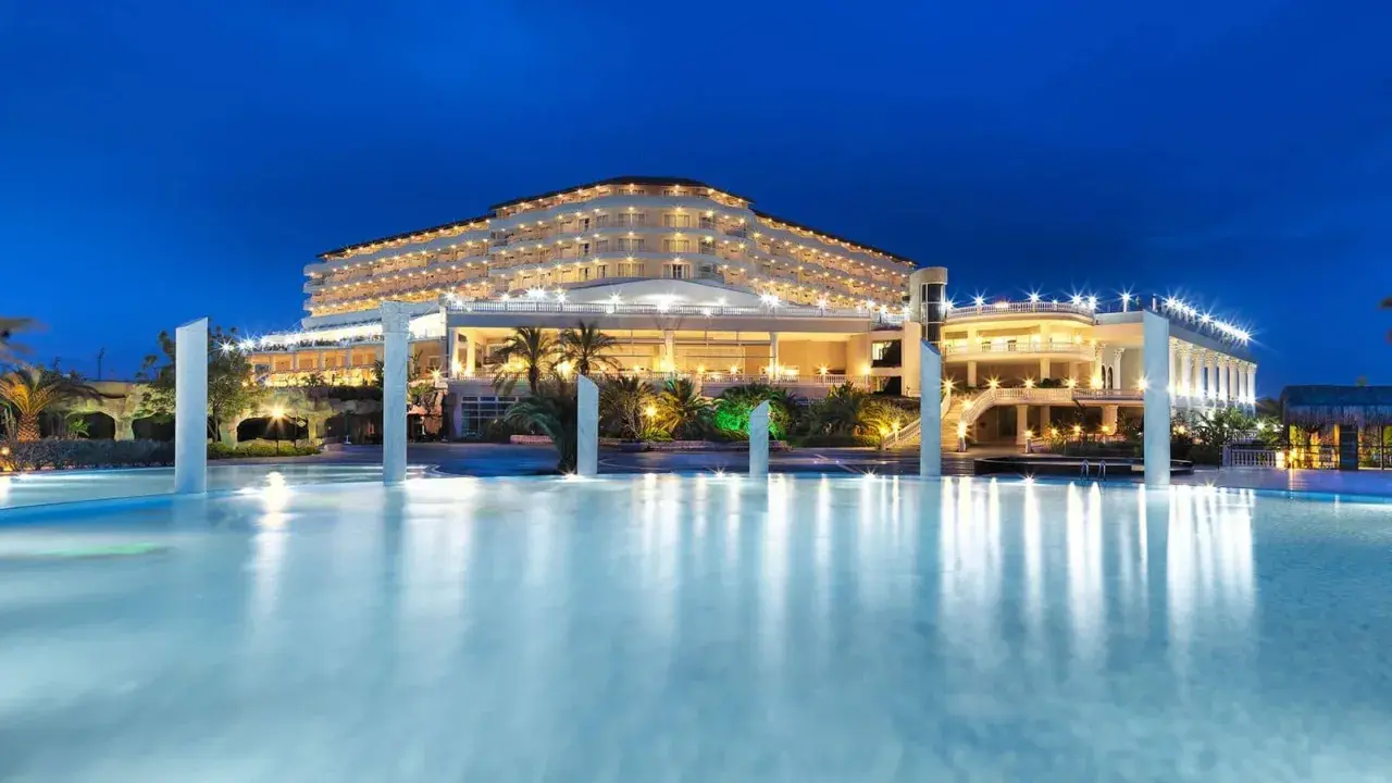 Elegancki Starlight Resort Hotel nocą, z oświetlonym basenem i palmami.