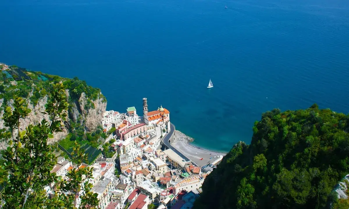 Vista dall'alto di Amalfi, con il mare blu e una barca a vela. La distanza tra Ravello e Amalfi è breve, ma il panorama è mozzafiato.