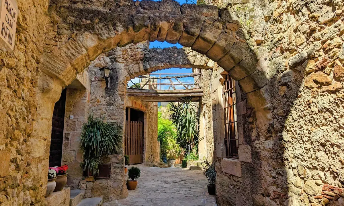 Antiker Durchgang in Pals, Spanien, mit steinernen Bögen und mediterraner Vegetation.