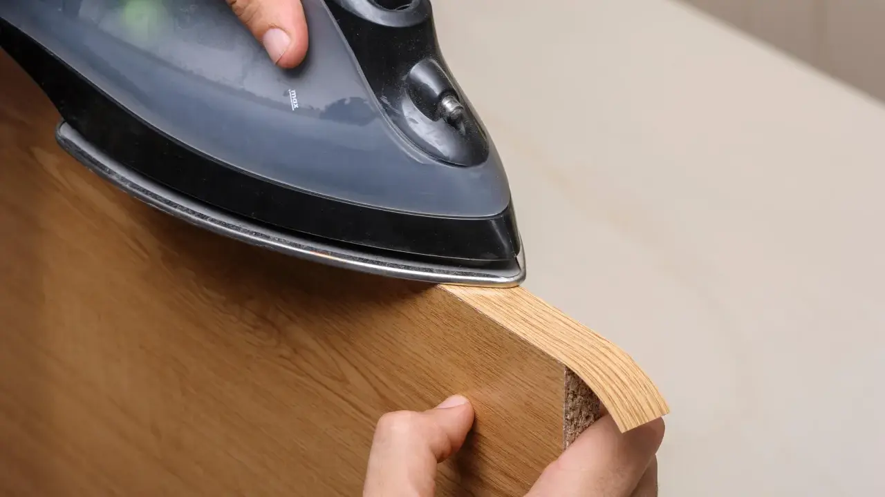 Persona aplica cinta de cantear a un borde de madera con una plancha.