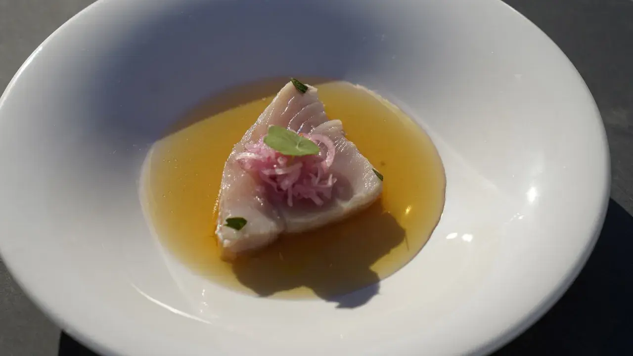 Bonito fresco en un caldo dorado, coronado con cebolla morada y una hoja verde. Un plato ligero y sabroso.
