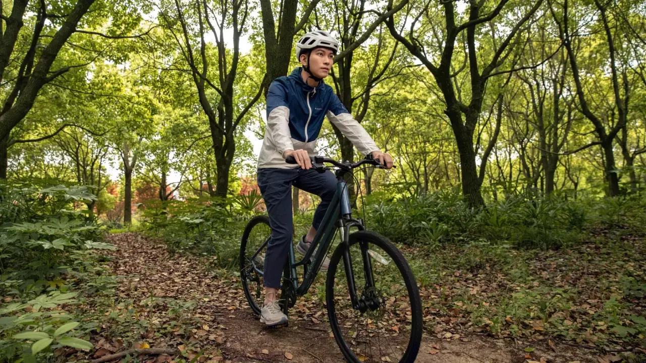 Mężczyzna w kasku jedzie rowerem trekkingowym po leśnej ścieżce. Taki rower to wszechstronny towarzysz podróży.