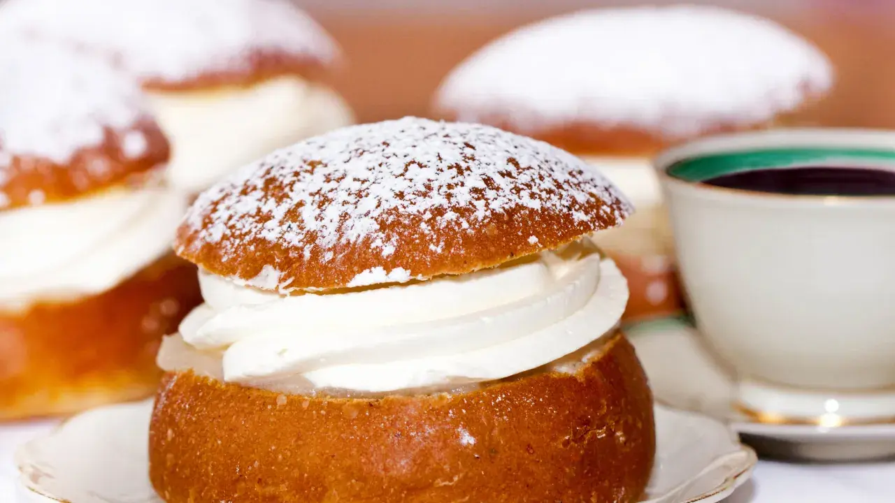 Semlor, en fest vid fastan, pudrade med florsocker och fyllda med grädde. En kopp kaffe i bakgrunden.