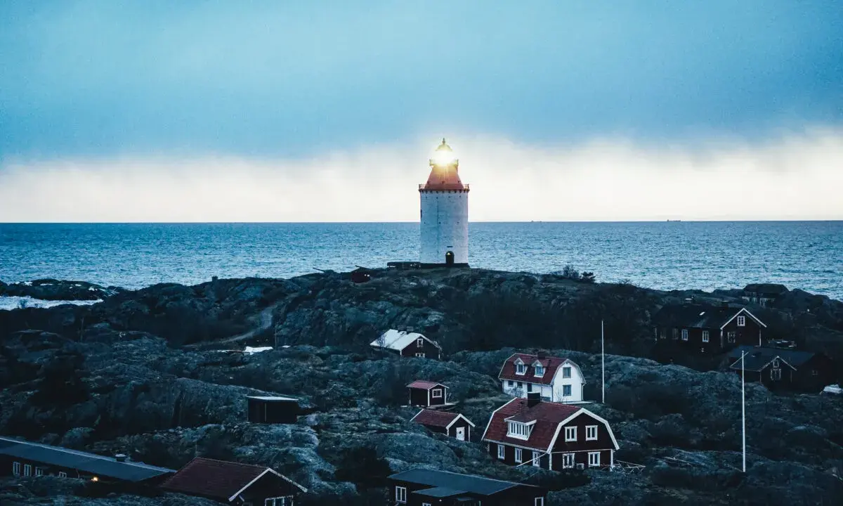 En fyr lyser över klippor och röda hus vid havet. En idyllisk plats för unika hotell Sverige.