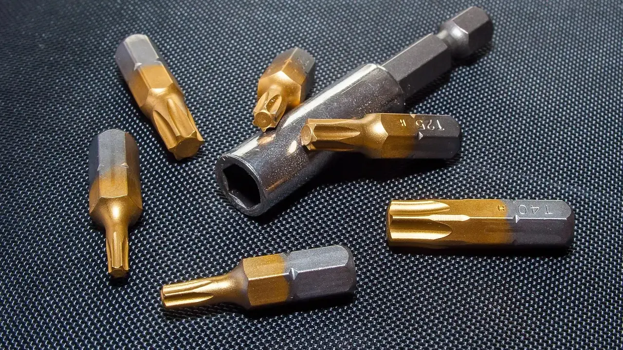 Różne rodzaje bitów Torx, w tym T25 i T40, leżą obok metalowego uchwytu na czarnym, teksturowanym tle.