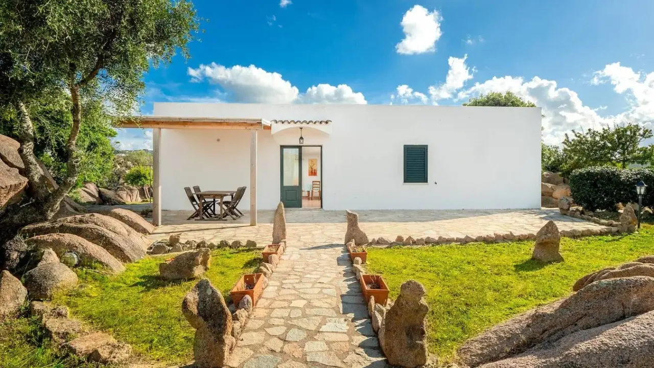 Un sentiero in pietra conduce a un bianco casolare, circondato da rocce granitiche e vegetazione mediterranea. Ideale per scoprire gli agriturismi Sardegna nord.