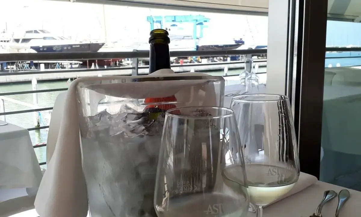 Un bicchiere di vino bianco e una bottiglia in un secchiello di ghiaccio, con vista sul porto e yacht, al ristorante club nautico Rimini.