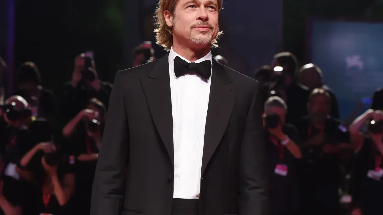 Brad Pitt looking dapper in a classic tuxedo with a black cummerbund and bow tie, posing for photographers.