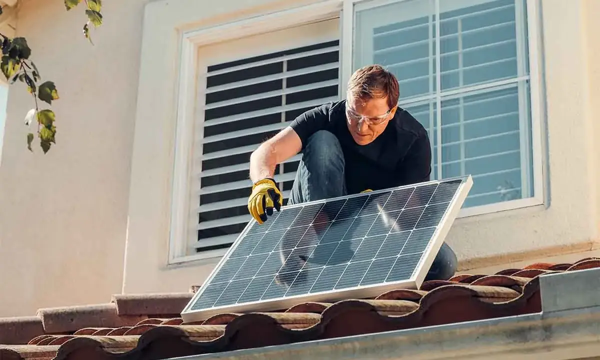Instalación de placas solares en comunidad de vecinos. Un hombre con guantes y gafas de seguridad coloca un panel solar en un tejado.
