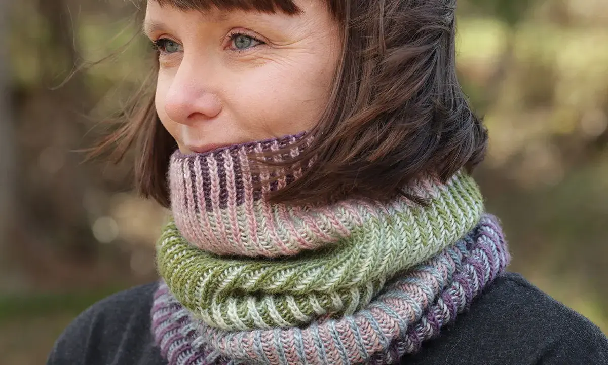 Woman wearing a colorful knitted cowl in shades of green, pink, and purple.