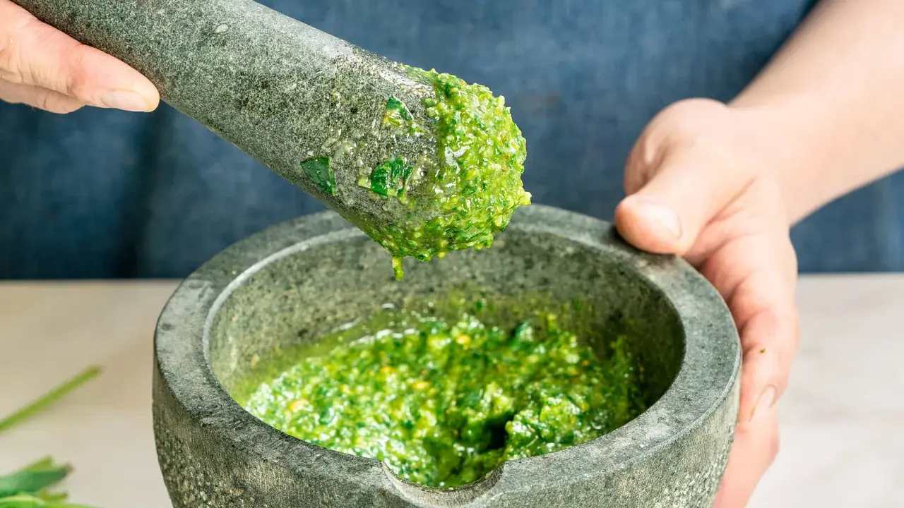 Frisches basilikum pesto wird in einem Mörser zerstoßen. Tropfen des grünen Pesto fallen vom Stößel in die Schüssel.