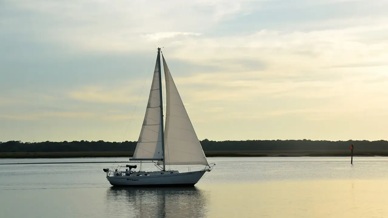 Un voilier blanc navigue sur une eau calme, ses voiles gonflées par le vent. La composition du bateau, avec la ligne d'horizon et le ciel doux, crée une scène paisible.