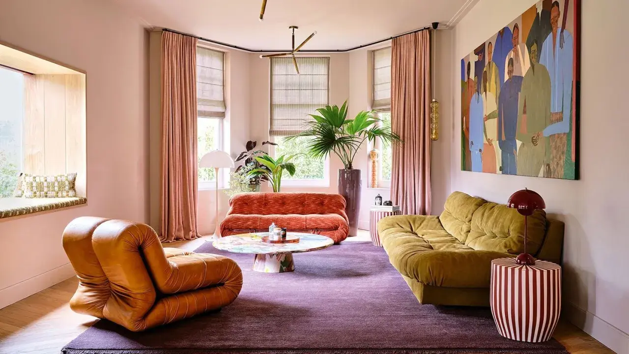 Comment amenager un salon : un fauteuil orange, un canapé rouille, un canapé moutarde, une table basse colorée, un tapis violet et une grande peinture.
