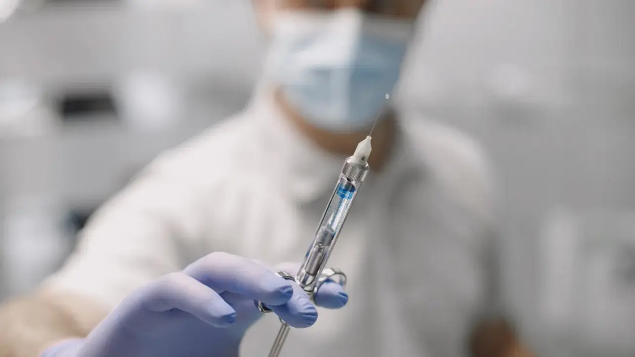 Dentysta w masce i rękawiczkach trzyma strzykawkę do znieczulenia nasiękowego.